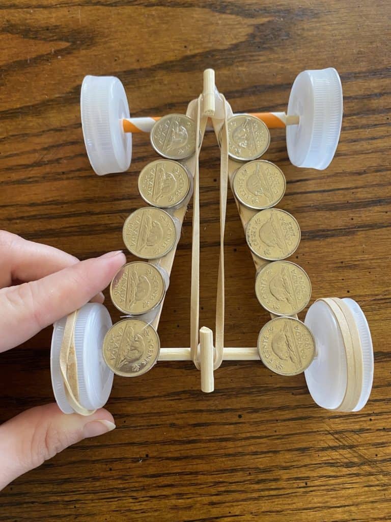 Coins laying on top of a race car made from popsicle sticks, straws, and bottle caps.