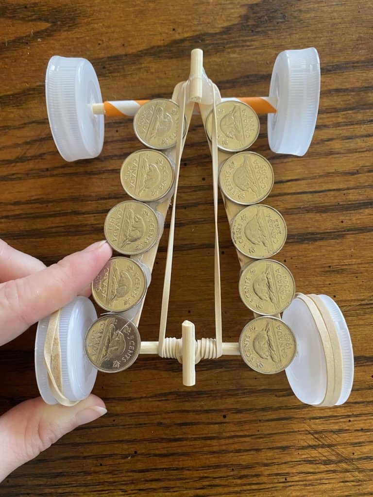 Coins laying on top of a race car made from popsicle sticks, straws, and bottle caps.