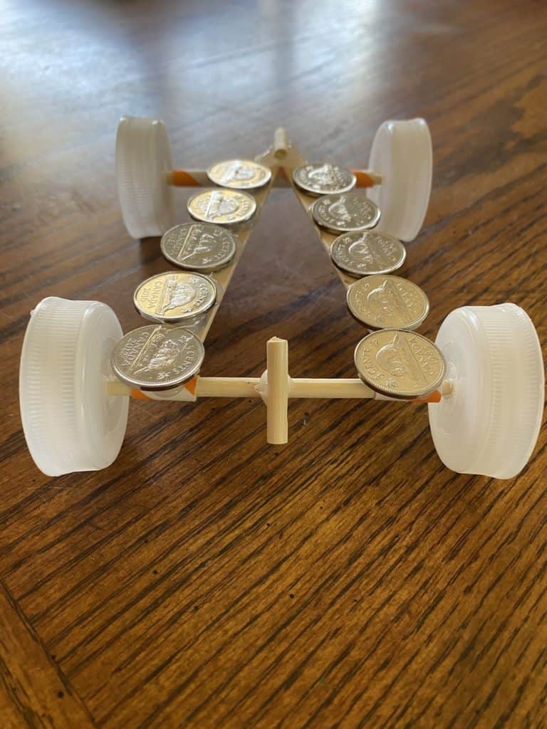 Coins laying on top of a race car made from popsicle sticks, straws, and bottle caps.