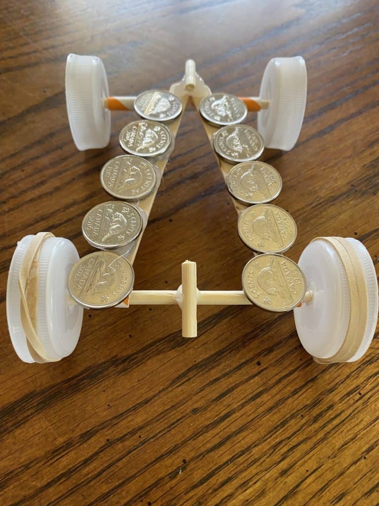 Coins laying on top of a race car made from popsicle sticks, straws, and bottle caps.