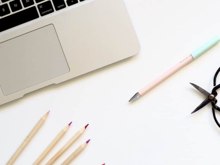 laptop open with pencils and a pen laying in front of it