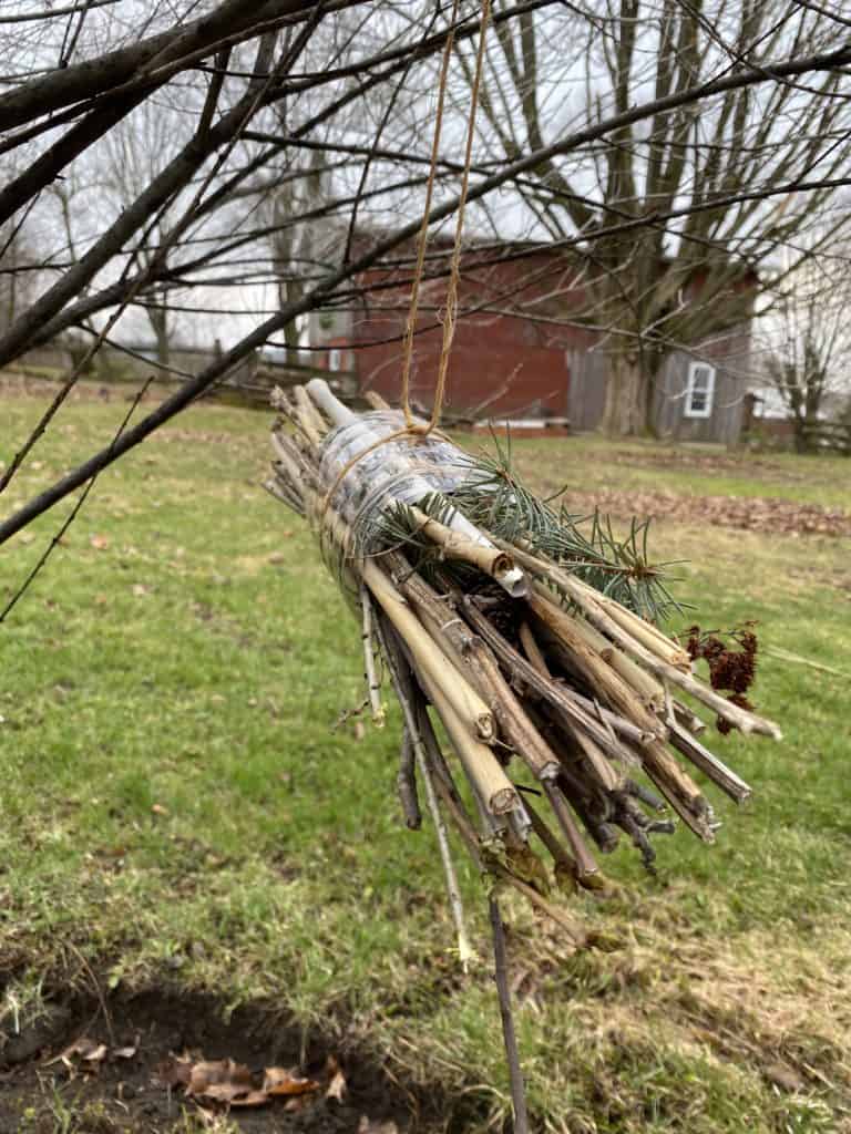 A bee hotel, created using recycled and natural materials, hanging outside on a tree.