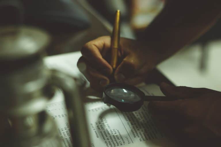 A person writing in a journal, also using a magnifying glass.