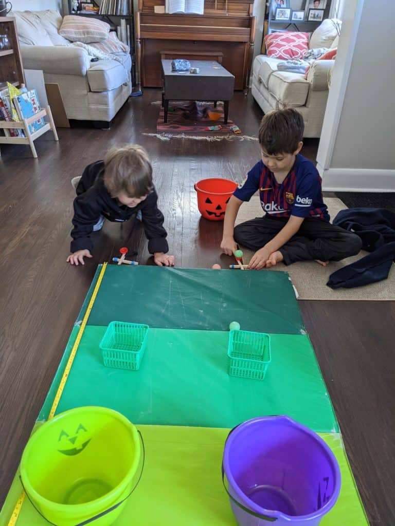 Two kids sitting in front of a green mat, using popsicle sticks to play a game.