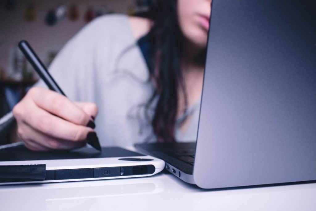 Woman using a drawing table, looking at a computer screen faced away from camera.