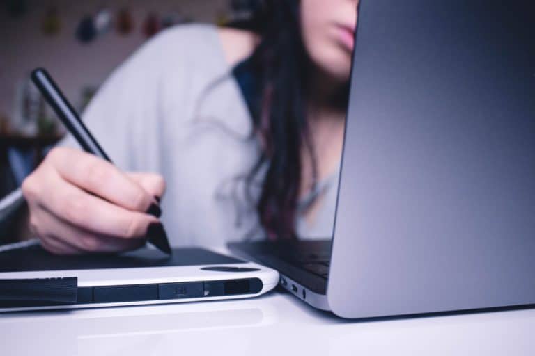 Woman using a drawing table, looking at a computer screen faced away from camera.