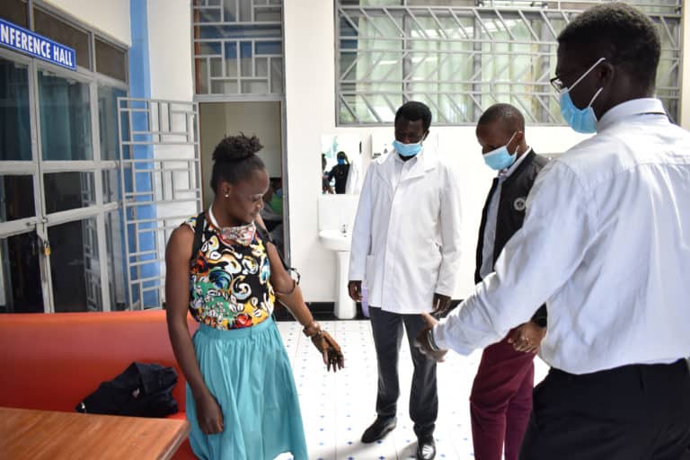 A woman standing to the left with a blue skirt on and a prosthetic arm, and 3 men standing to the right