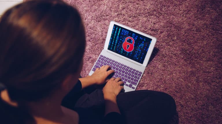 Person sitting cross-legged on the ground using a laptop with a large red lock on the screen.