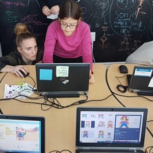 A makerspace staff helping a student do their work while running a course. Scrach is on the screens.