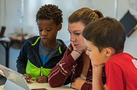 Two students and an educator looking at a tablet.