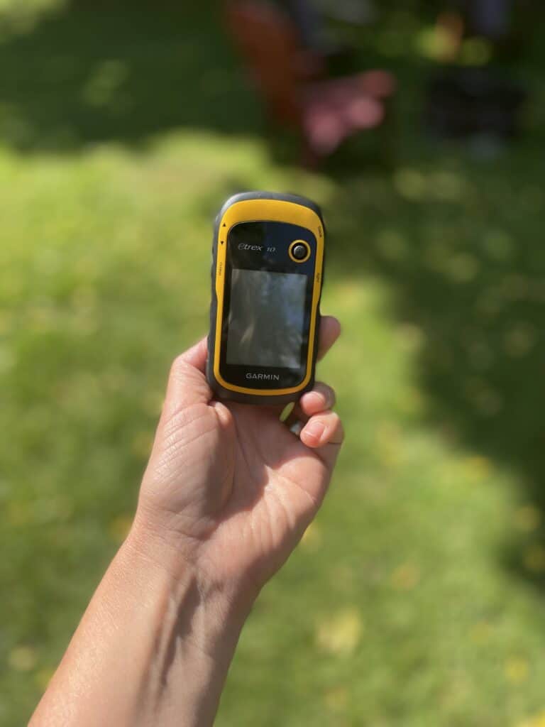 Someone holding a GPS in their hand outside. Grass can be seen in the background.