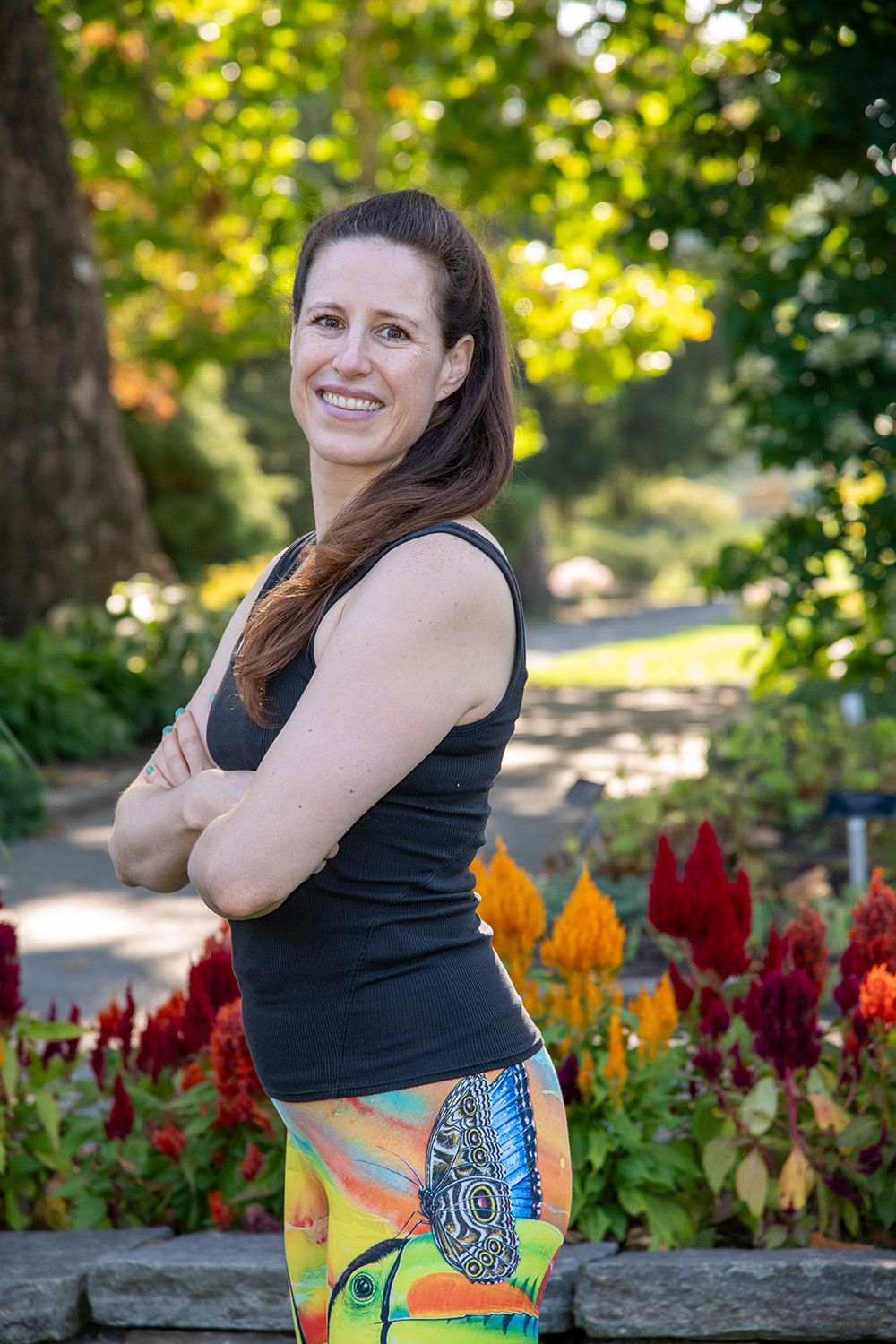 A portrait of Carolanne Black standing sideways, with flowers behind.