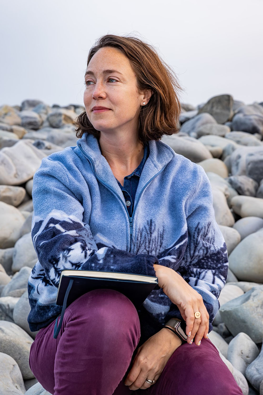 A portrait of Karen Pinchin, she is sitting on rocks, looking off to the left.